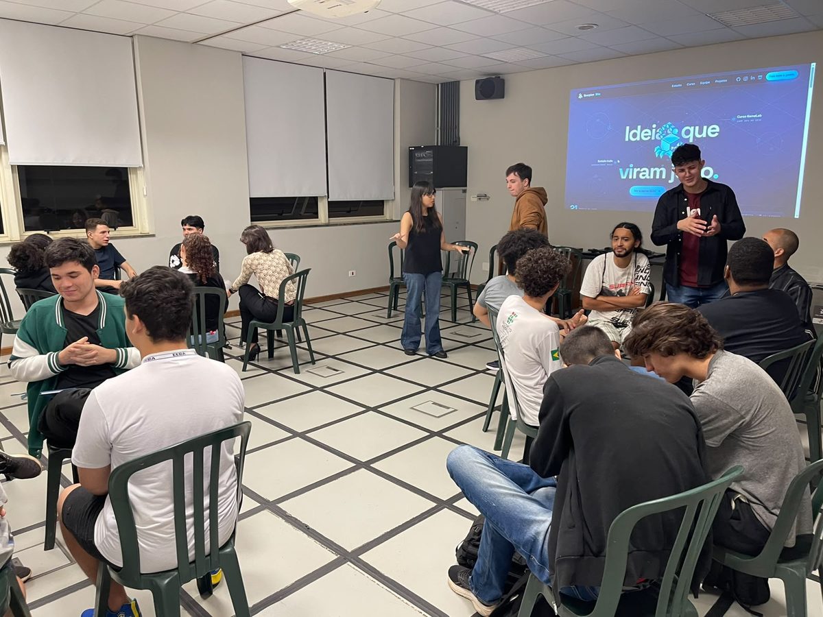 Turma do GameLab sentada em roda no SESC Araraquara, com o site da Scorpion Bits projetado na parede ao fundo.